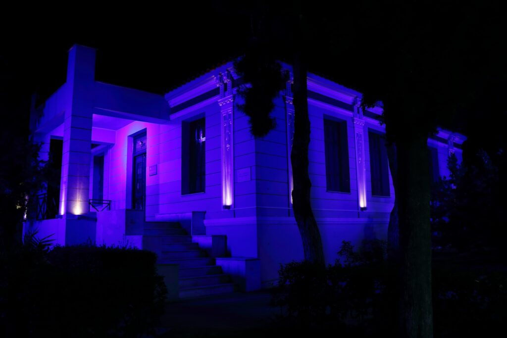 Είσοδος και πλαϊνή όψη με μπλε και μωβ φωτισμό Είσοδος και πλαϊνή όψη με μπλε και μωβ φωτισμό / Entrance and side façade with blue and purple lighting